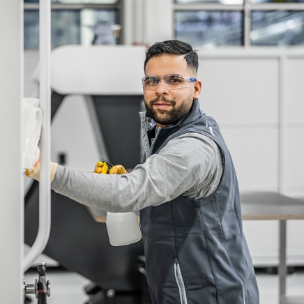 Lächelnde männliche Reinigungskraft mit Schutzbrille bei der Reinigung einer Maschine