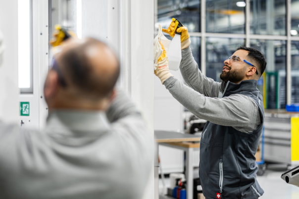 Zwei männliche Reinigungskräfte mit Schutzbrillen reinigen in einer Industriehalle