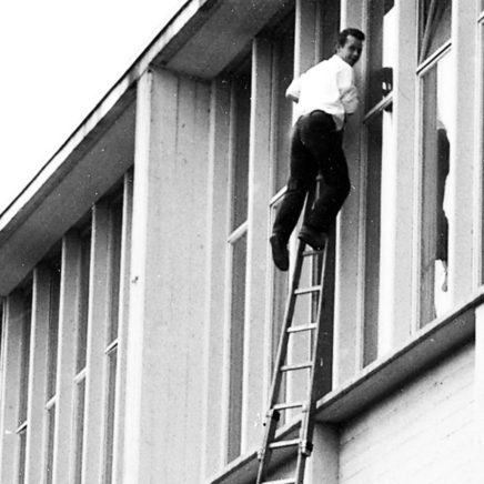 Mann auf Leiter am Fenster vor altem Conradygebäude