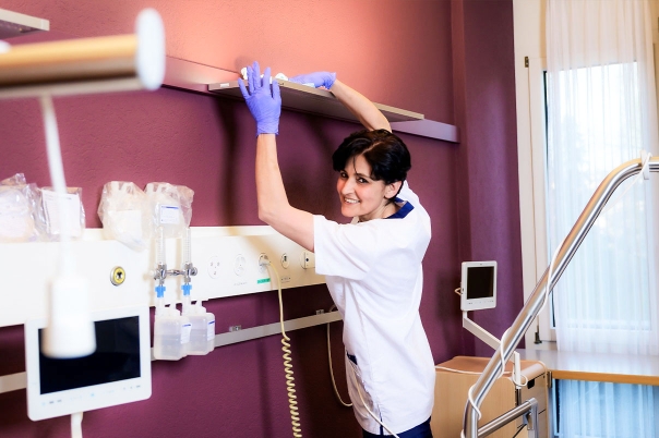 Weibliche Reinigungskraft mit weißem T-Shirt reinigt Regal in Krankenzimmer