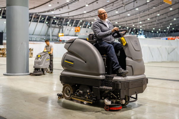 Männliche Reinigungskraft auf großem, fahrbaren Bodenreiniger in Messehalle