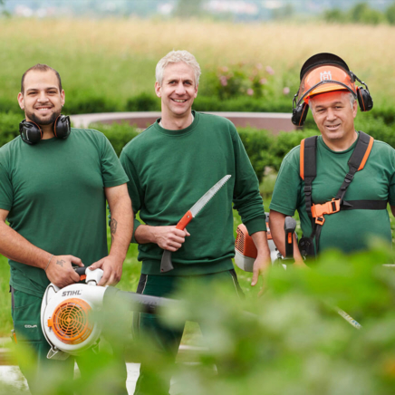 Drei Mitarbeiter der Conradygruppe bei der Pflege von Außenanlagen mit Helm, Säge und Laubbläser