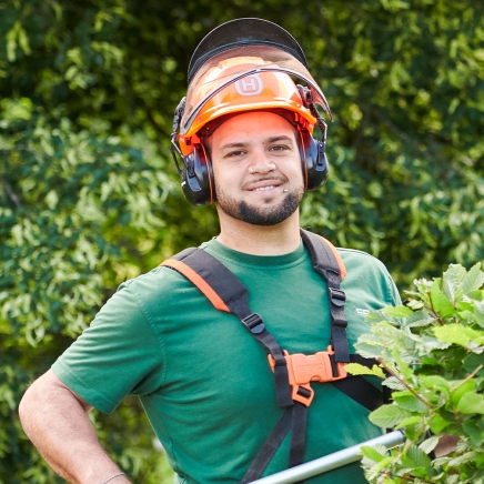 Männliche Reinigungskraft mit orangenem Schutzhelm bei der Außenpflege eines Parks