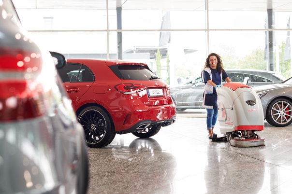 Weibliche Reinigungskraft mit kleiner Bodenreinigungsmaschine reinigt Autohaus