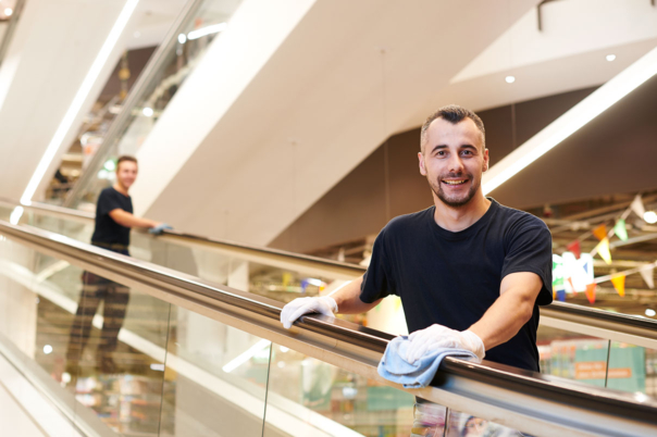 Zwei junge männliche Reinigungskräfte reinigen Rolltreppe in Einkaufszentrum