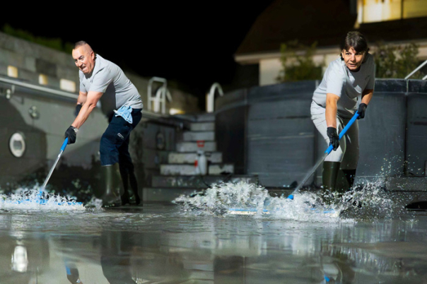 Weibliche REinigungsmitarbeiter und männlicher Reiniungsmittarbeiter entfernen Restwasser mit Wasserschieber aus einem Schwimmbecken im Rahmen einer Beckenreinigung, Sonderreinigung.