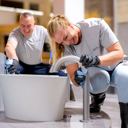 Weibliche Reinigungsmitarbeiterin und männlicher Reinigungsmitarbeiter reinigen Fussbad in einer Saunaanlage.